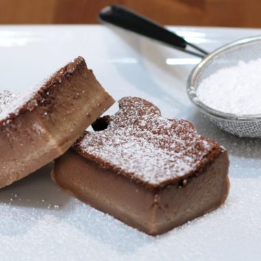 chocolate magic cake slices on a white plate next to powdered sugar