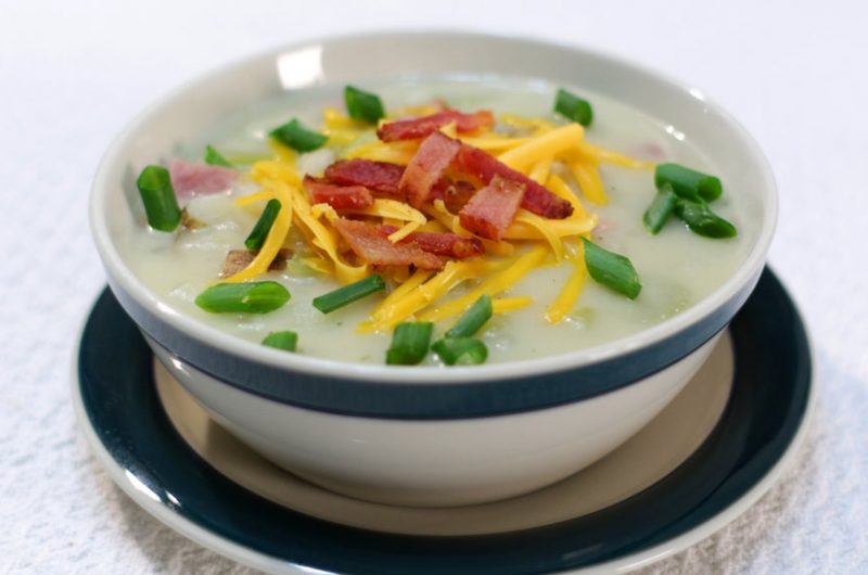 Ham and potato soup topped with bacon and cheese in a bowl.