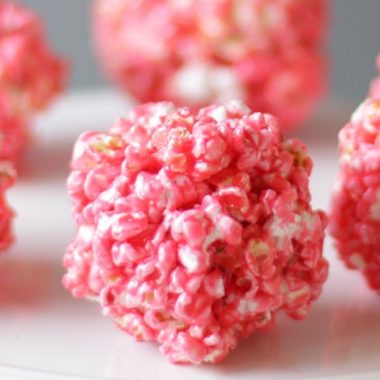 several pink popcorn balls on a white plate.