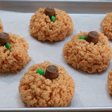 Pumpkin rice krispies treats on a sheet pan with parchment paper.