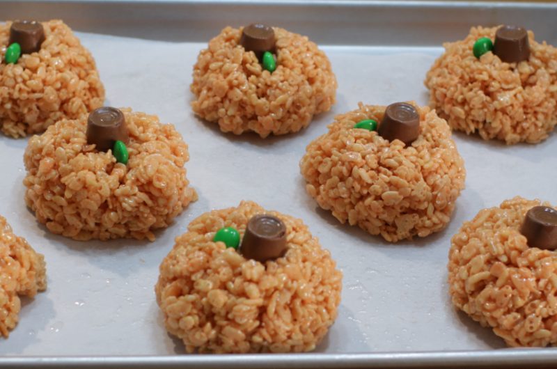 Pumpkin rice krispies treats on a sheet pan with parchment paper.