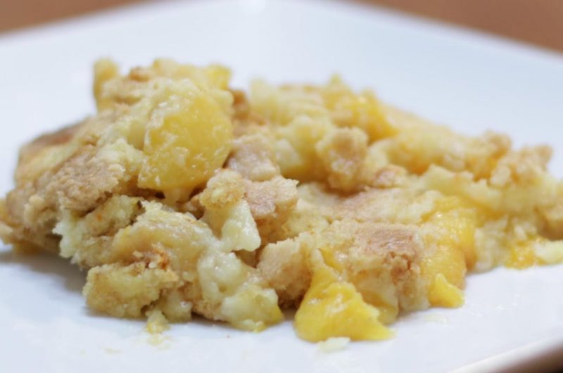 White plate with a mound of cake mix peach cobbler on it.