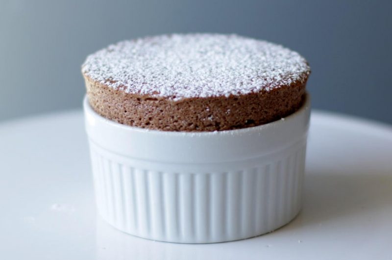 Easy chocolate souffle on a white cake pedestal in a white ramekin