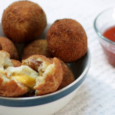 Several bacon and cheese mashed potato balls in a bowl on a table.