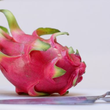 Dragon fruit on a white cutting board with a knife.