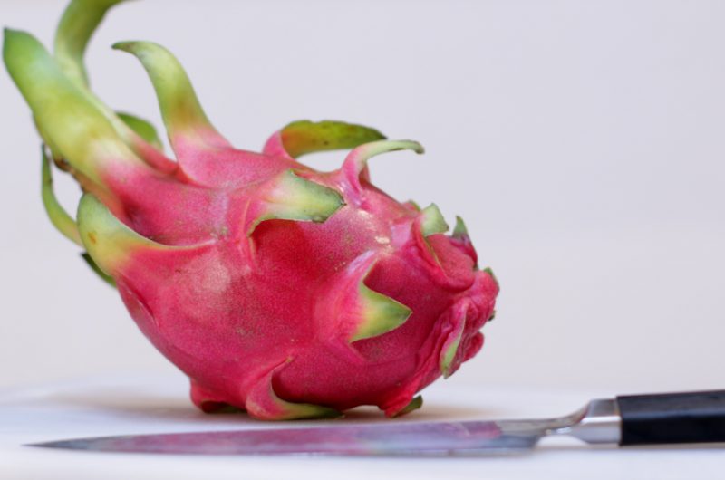Dragon fruit on a white cutting board with a knife.