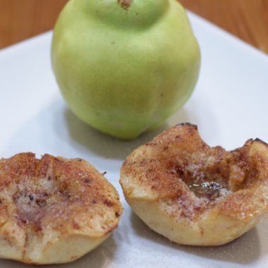 Quince fruit next to two slices of baked quince on a white plate