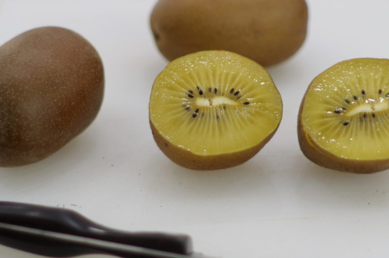 Kiwi gold cut in half on a white cutting board