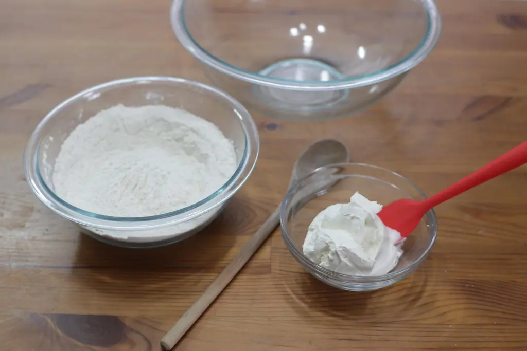 Flour and sour cream in bowls on a wooden table.