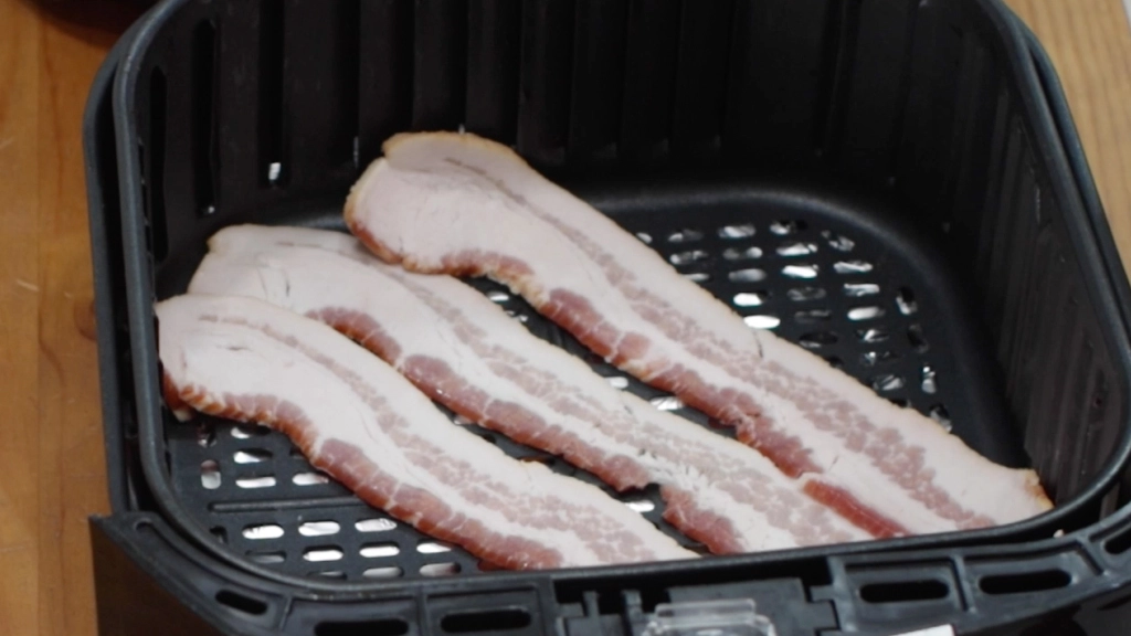 3 slices of thick-cut bacon in an air fryer basket.