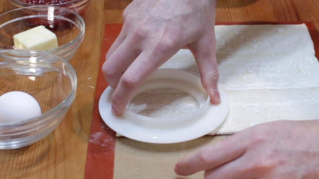 Hand with round cutter cutting circle out of puff pastry sheet.