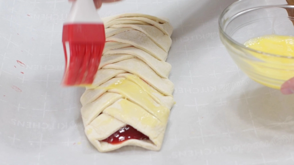 Pastry brush basting egg wash on top of a braided puff pastry.