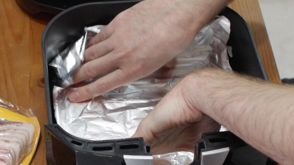 Hand placing foil in the bottom of an air fryer basket.