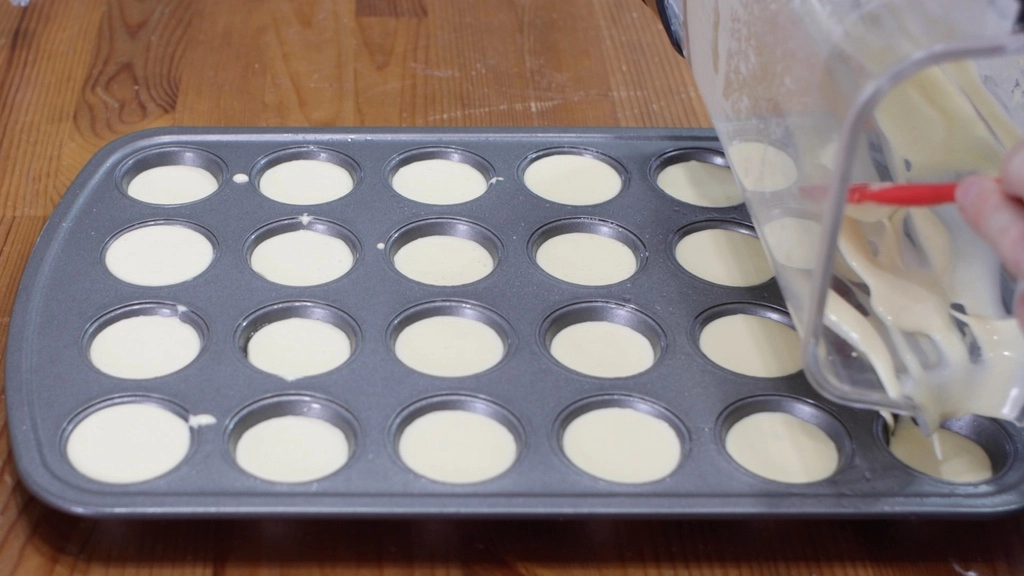 Blender pouring Brazilian cheese bread batter into a mini muffin pan.