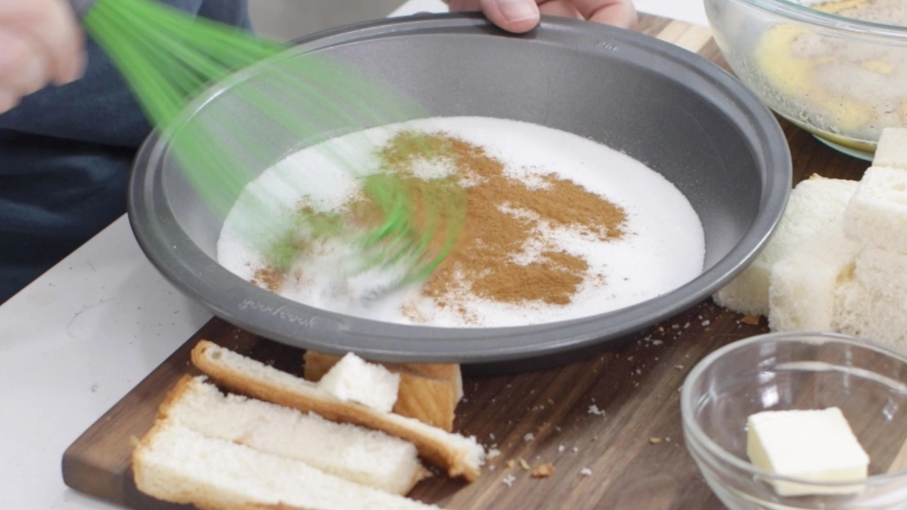 Hand whisking cinnamon and sugar in a pie plate.