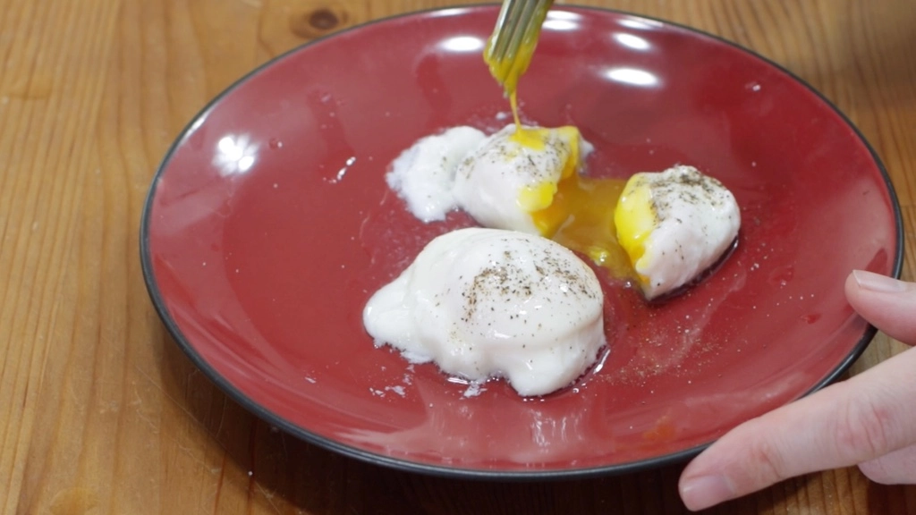 Fork breaking apart a poached egg on a red plate.