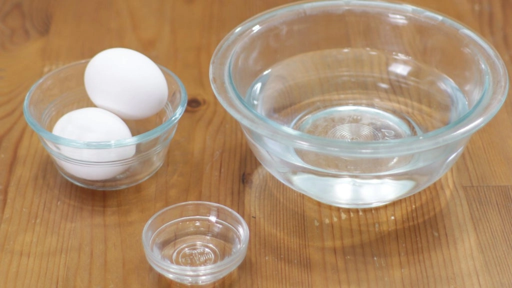 Two eggs and other ingredients in glass bowls on a wooden table.