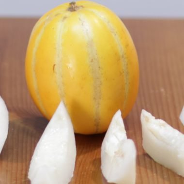 Korean melon on a wooden table with sliced melon in front of it.