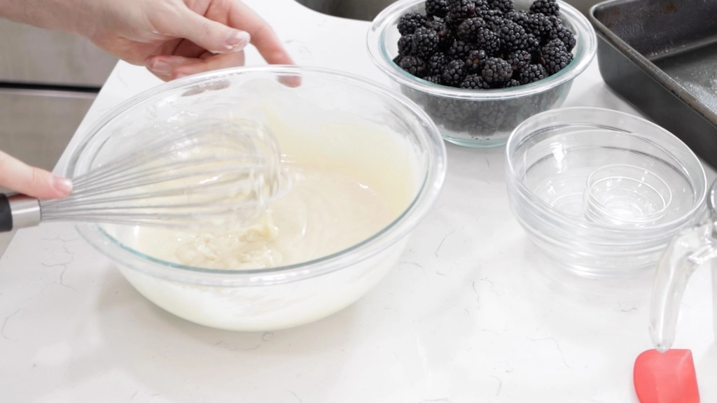 Hand whisking blackberry cobbler batter in a medium glass bowl.