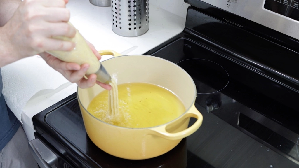 Hand piping the churros dough into a large pot of hot oil.