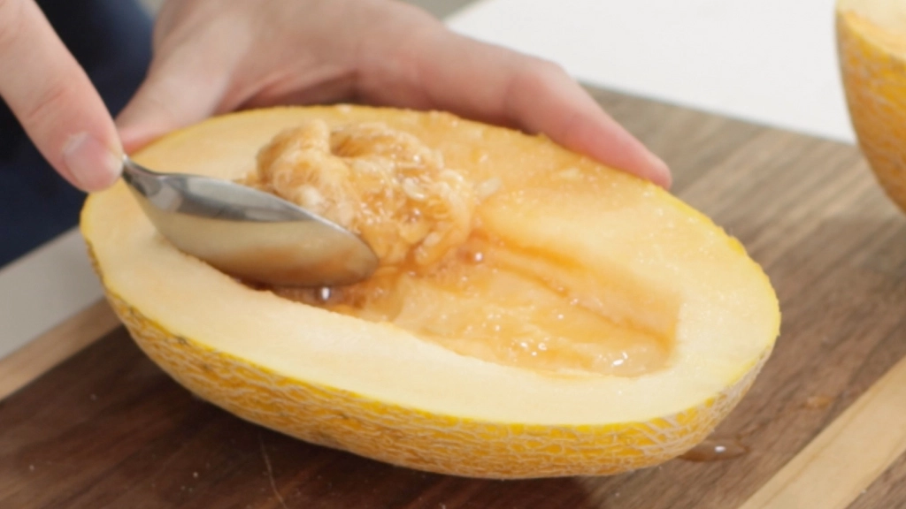 Spoon scooping out the seeds from the half of a hami melon.