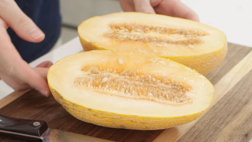 Sliced in half hami melon on a wooden cutting board.