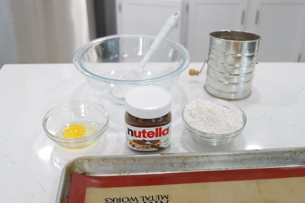 Three ingredients, egg, Nutella, and flour on a countertop.