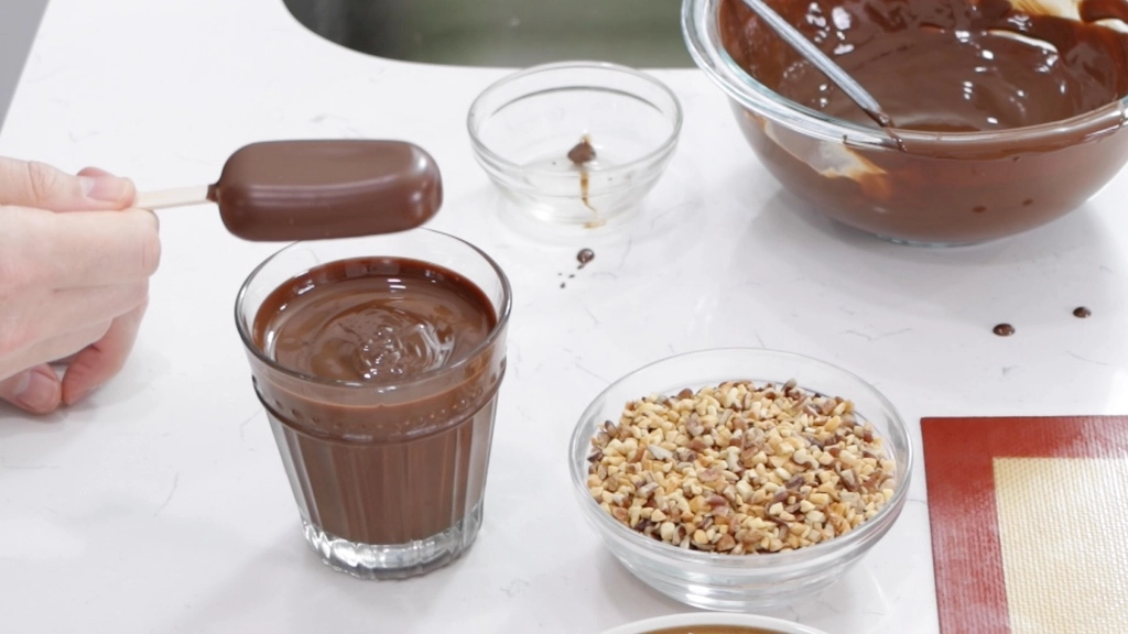 Ice Cream Bars Recipe | 5 Ingredients - In The Kitchen With Matt 7 Hand holding a chocolate dipped ice cream bar over a glass of chocolate.