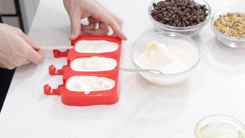 Ice Cream Bars Recipe | 5 Ingredients - In The Kitchen With Matt 4 Handing sticking a popsicle stick in a red ice cream bar mold.