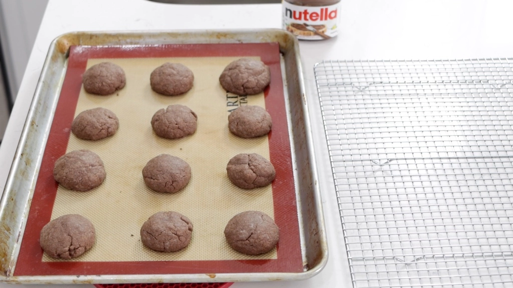 Freshly baked Nutella cookies next to a wire rack.