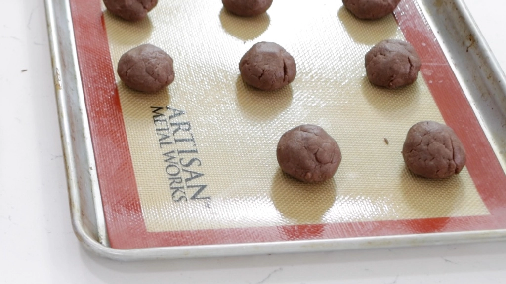 Balls of Nutella cookie dough on a sheet pan with a silicone baking mat.