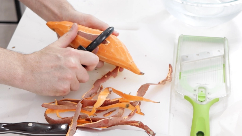 Hand peeling a sweet potato.