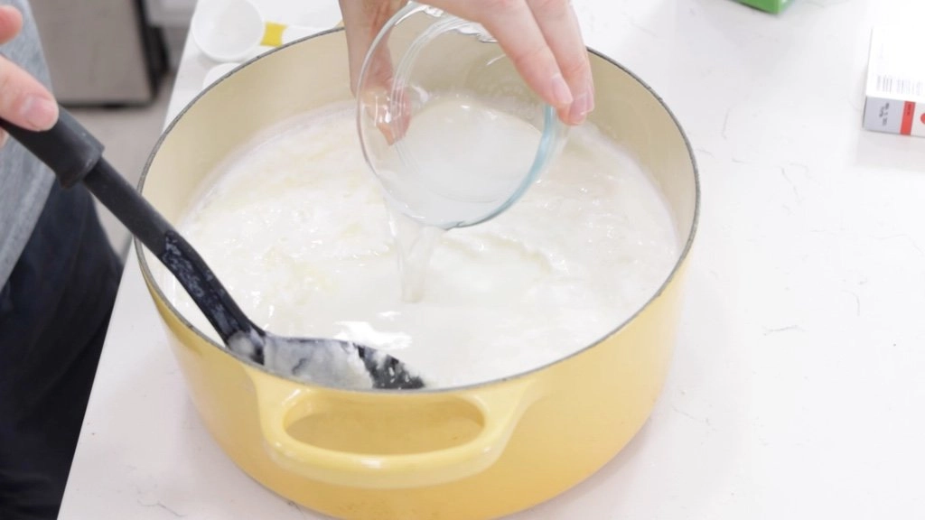 Pouring rennet into a pot of milk.