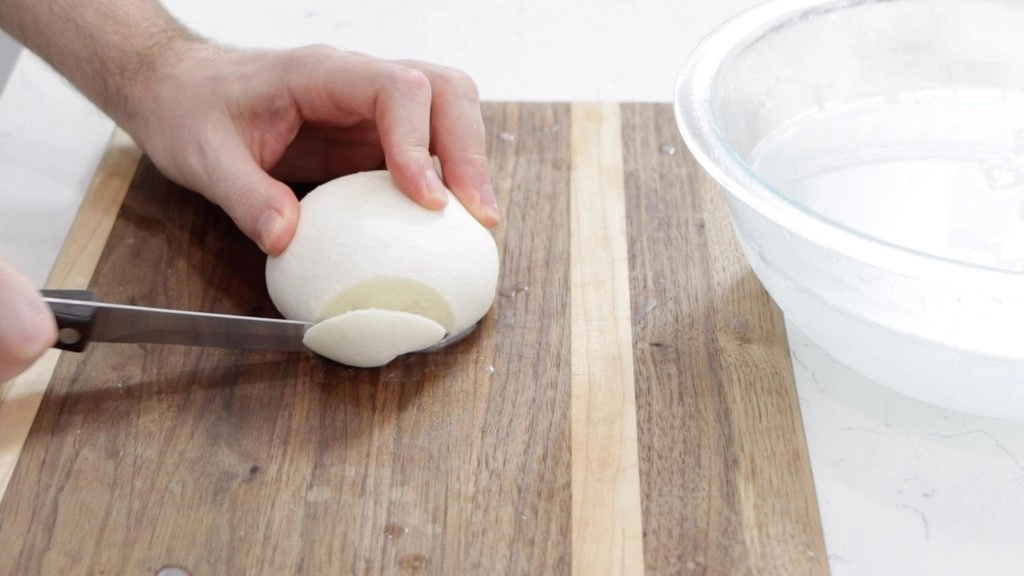 Hand slicing a ball of mozzarella cheese.