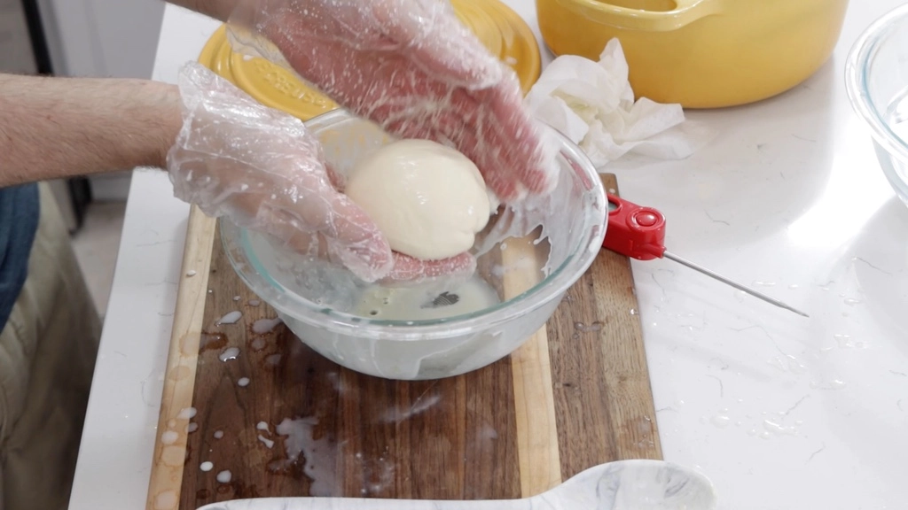 Hands shaping homemade mozzarella cheese into a ball.