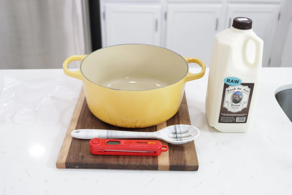 Raw milk next to a large yellow pot on a white counter top.