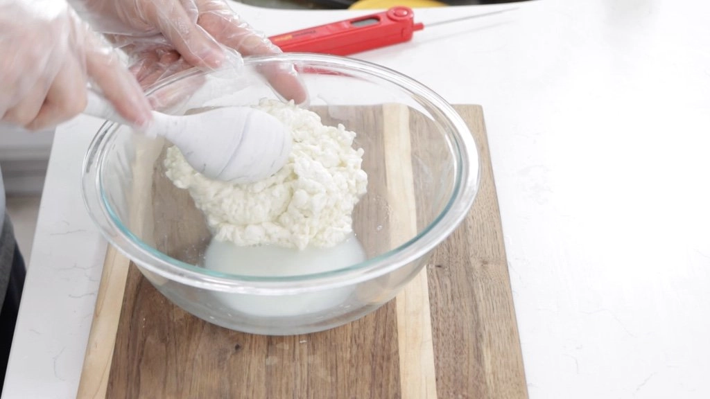 Spoon pressing against mozzarella cheese, releasing whey.