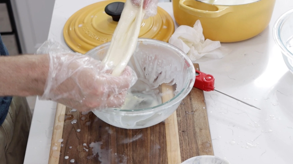 Hands stretching homemade mozzarella cheese over a bowl.