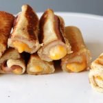 Pile of grilled cheese roll ups on a white plate.