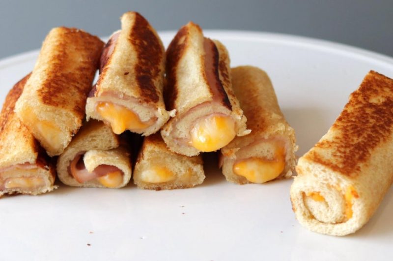 Pile of grilled cheese roll ups on a white plate.