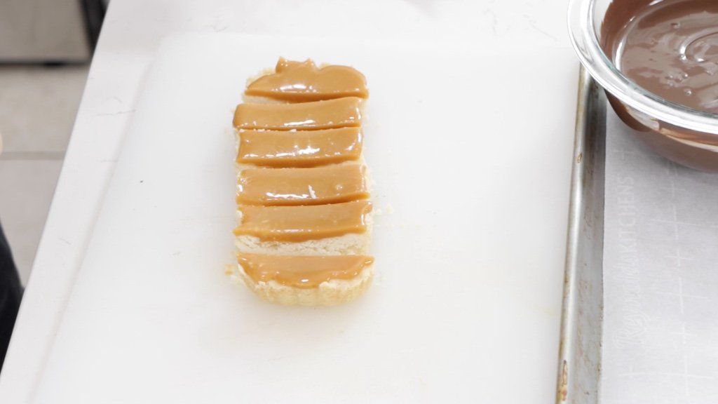 Caramel and shortbread cookie bars cut into bars on a white cutting board.