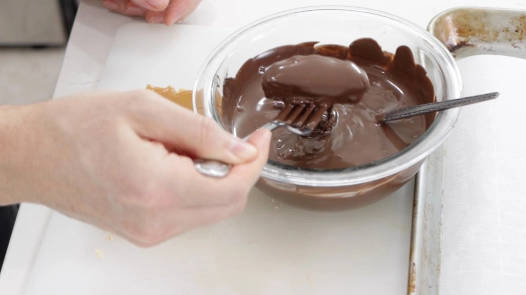 Hand with fork dipping a homemade Twix bar in a bowl of chocolate