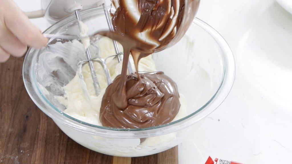 Melted chocolate being added to a bowl of cream cheese.
