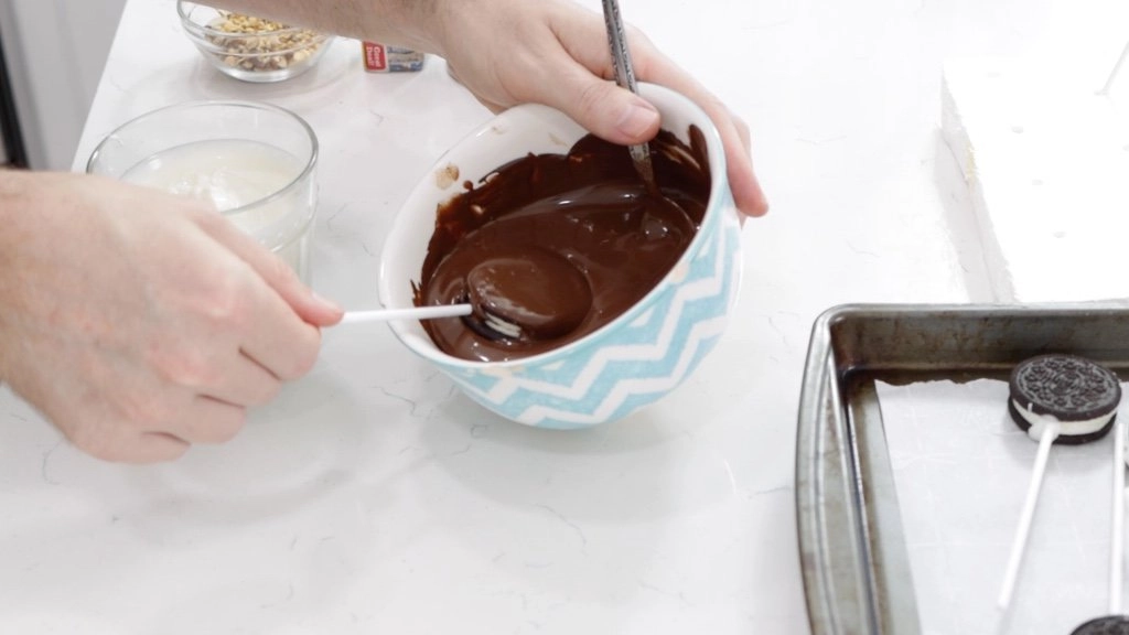 Hand tilting an Oreo pop in bowl of semi-sweet chocolate.