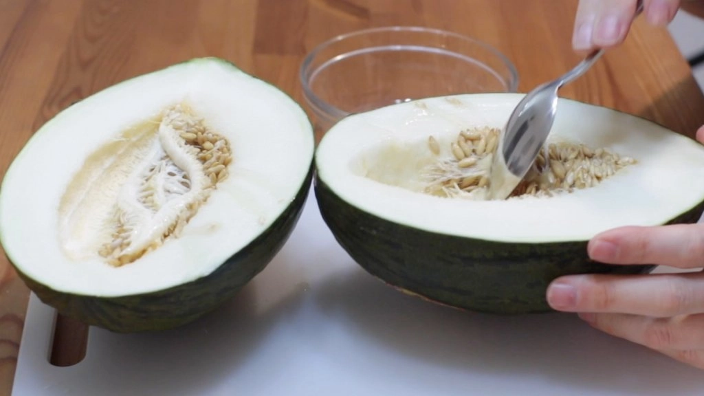 Hand scooping out seeds of a Santa clause melon with a spoon.