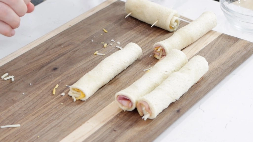 Several uncooked grilled cheese roll ups on a wooden cutting board.