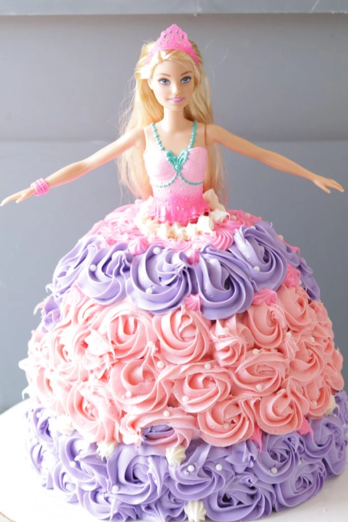 Barbie cake on a white cake pedestal with pink and purple flower dress.
