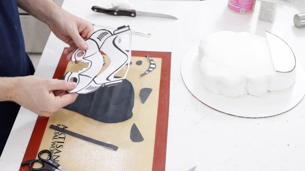 Hand holding a star wars cake stormtrooper head stencil with pieces cut out of it.