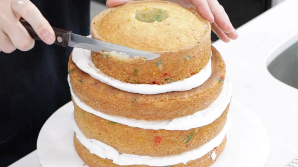 Hand with knife trimming a layered cake.