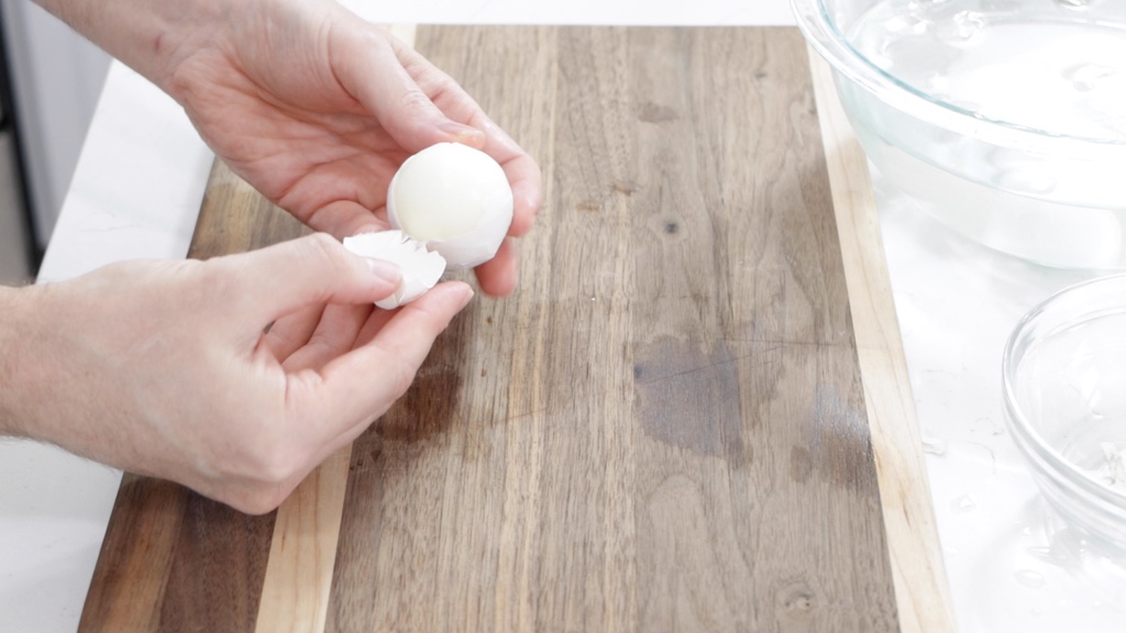 Hands peeling a hard-boiled egg.